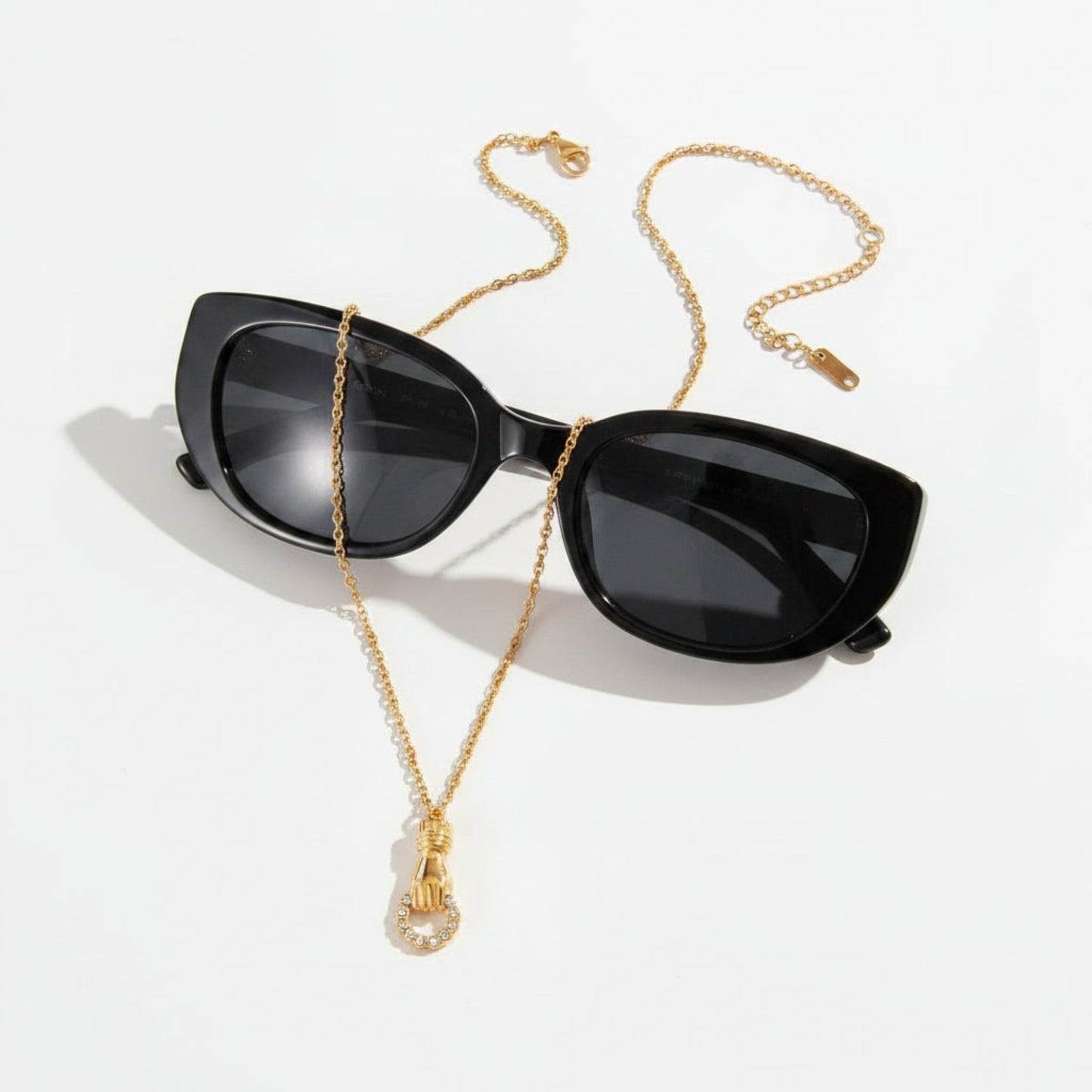 Black cat-eye sunglasses with a gold chain necklace strap featuring a small gold pendant, displayed on a clean white background.