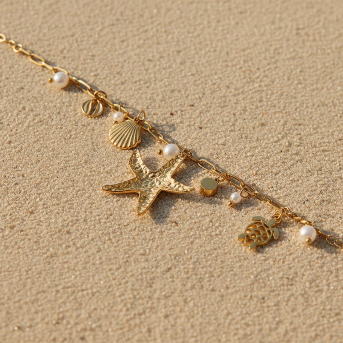 A gold-toned chain bracelet with sea-themed charms, including a starfish, seashells, a turtle, and small pearl beads