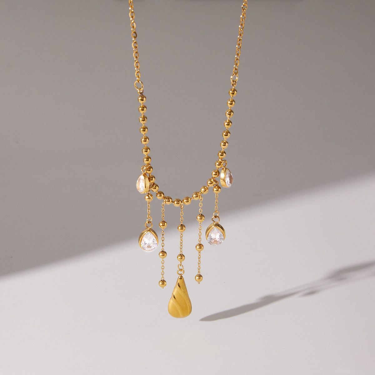 Gold necklace with hanging droplet pendants on a gradient background