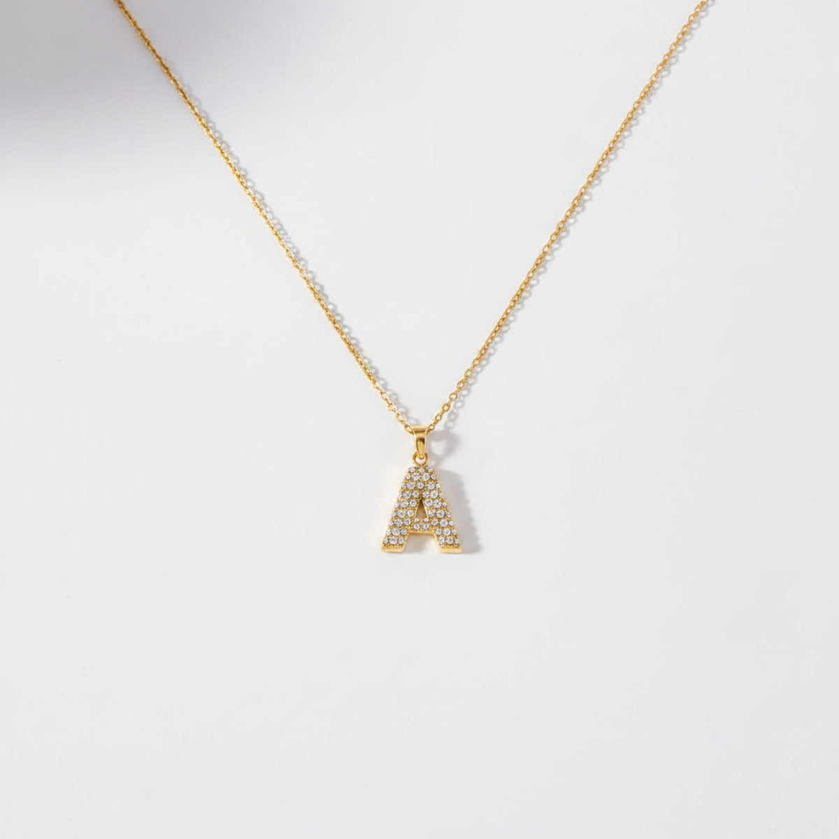 Gold necklace with a pendant on a light gray surface with cosmetic products.
