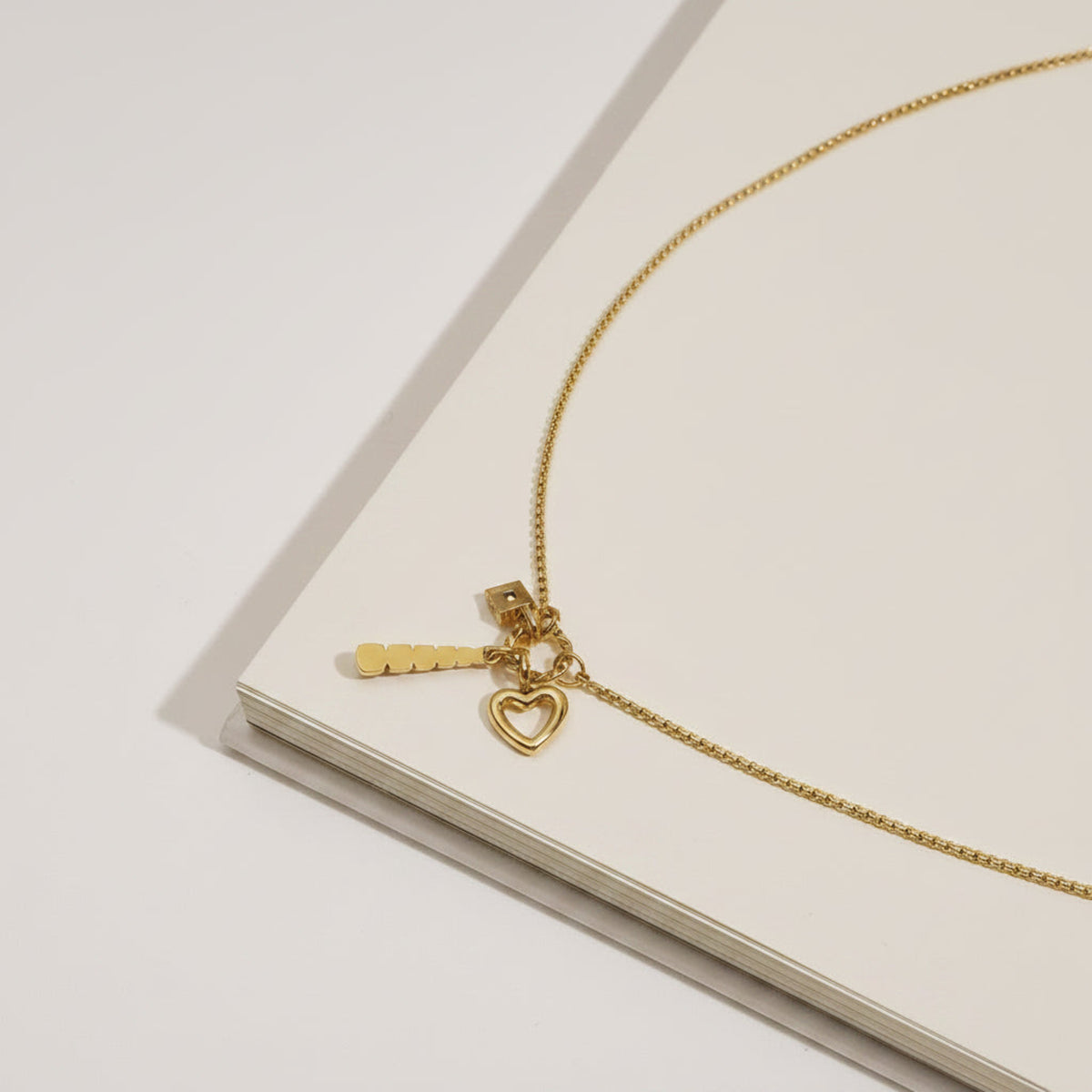 Gold necklace with heart charm on a yellow surface next to a halved orange and textured yellow fabric.