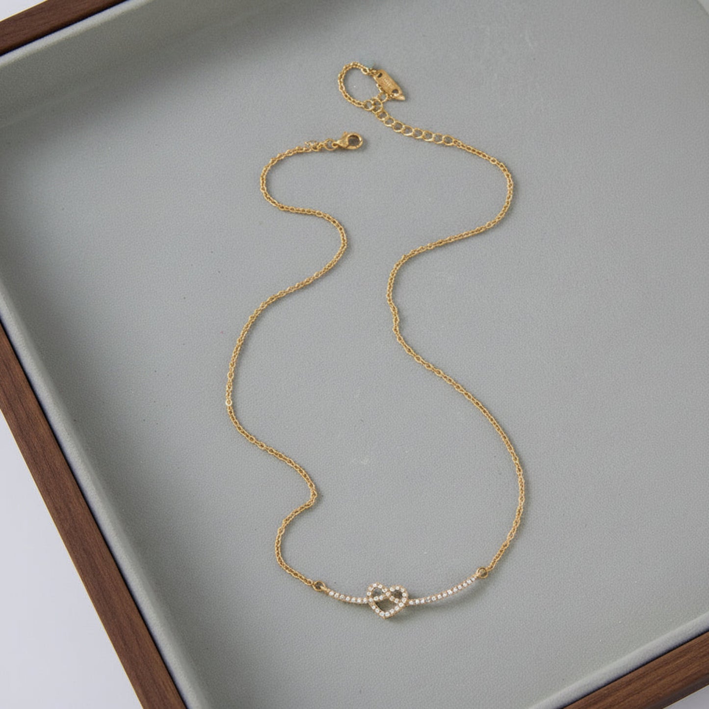 A delicate gold chain necklace with a small pearl knot centerpiece, displayed on a light gray jewelry tray.