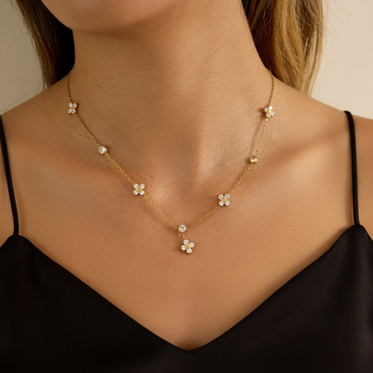 Gold necklace with floral pendants worn by a person in a beige sweater.