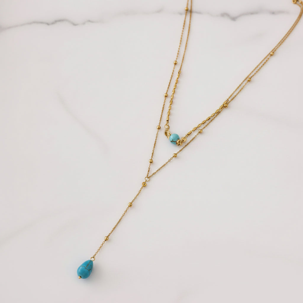 A gold double-strand necklace with small bead details and two turquoise blue teardrop beads