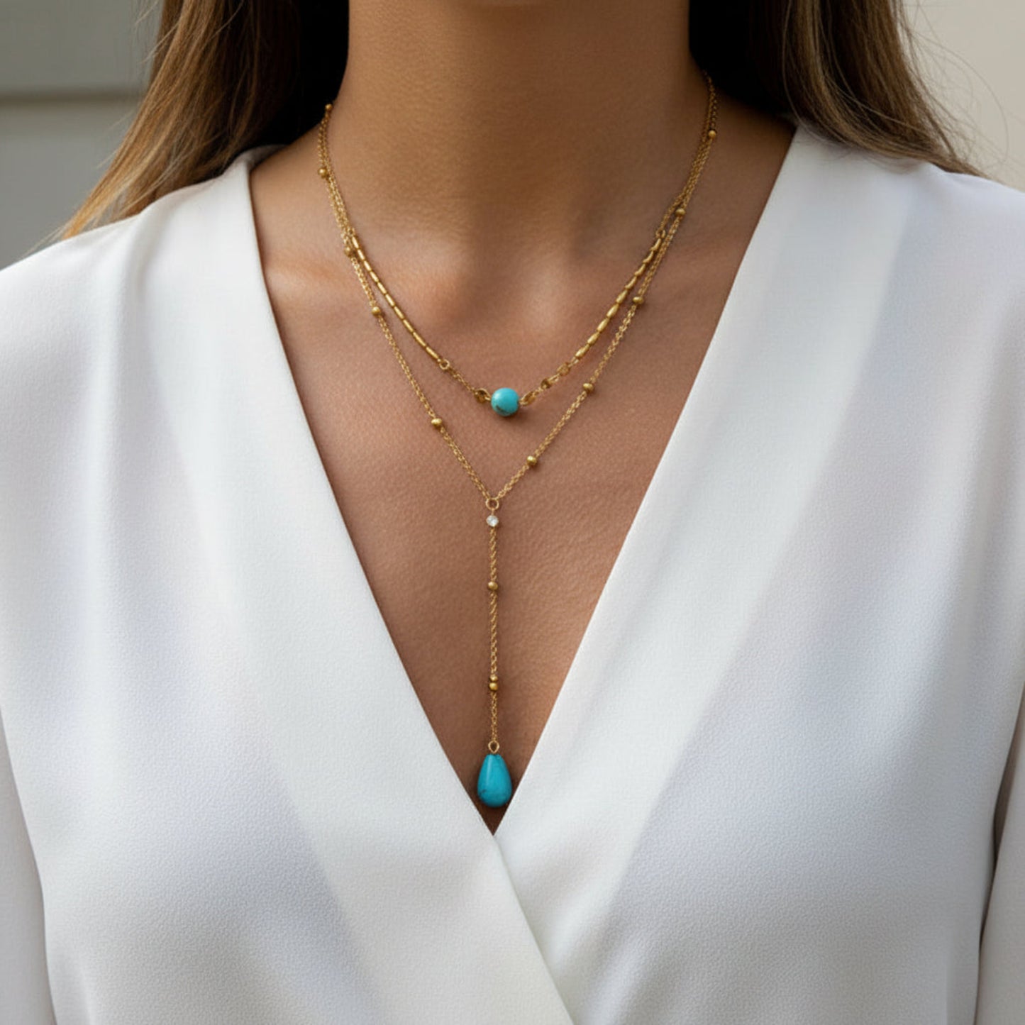 A close-up of a model wearing a gold double-strand lariat necklace with turquoise blue bead accents, 