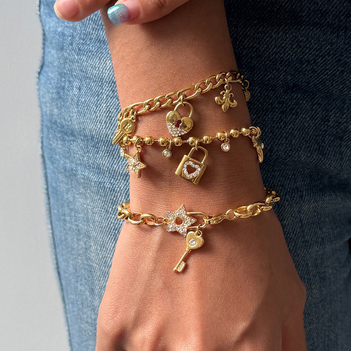 Gold bracelets with charms on a wrist against a denim background