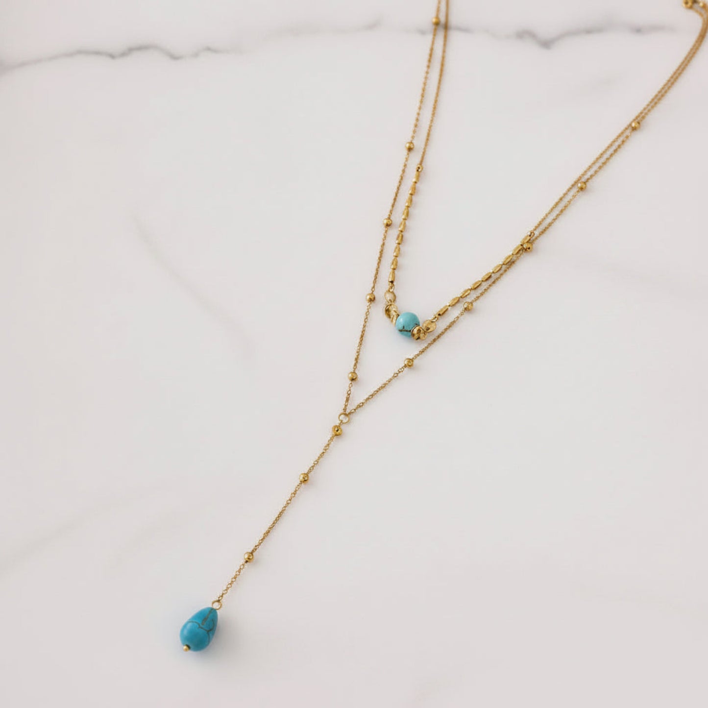 A gold double-strand necklace with small bead details and two turquoise blue teardrop beads