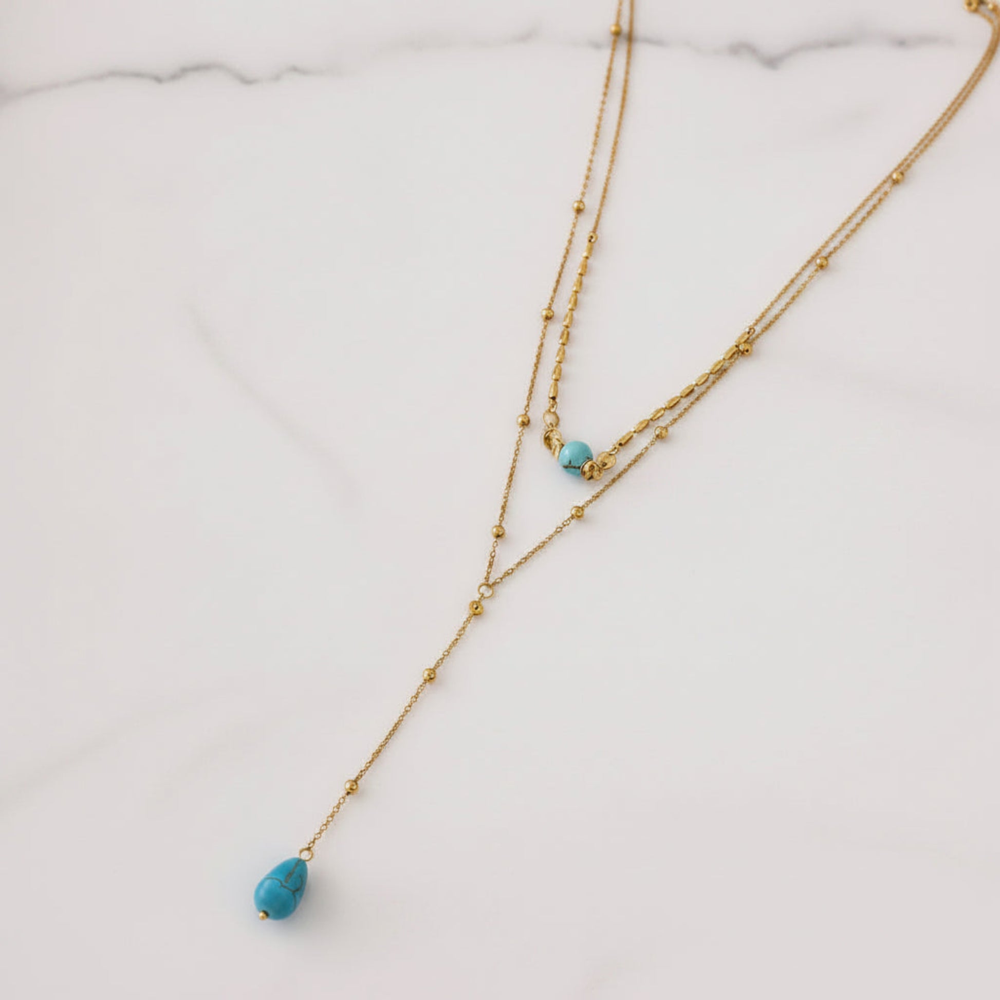 A gold double-strand necklace with small bead details and two turquoise blue teardrop beads