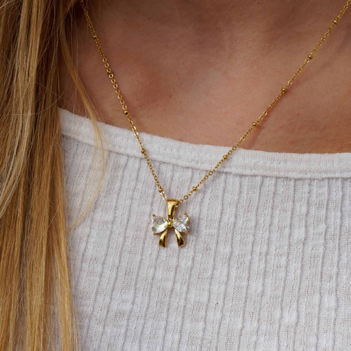 Gold necklace with a bow-shaped pendant worn by a person.