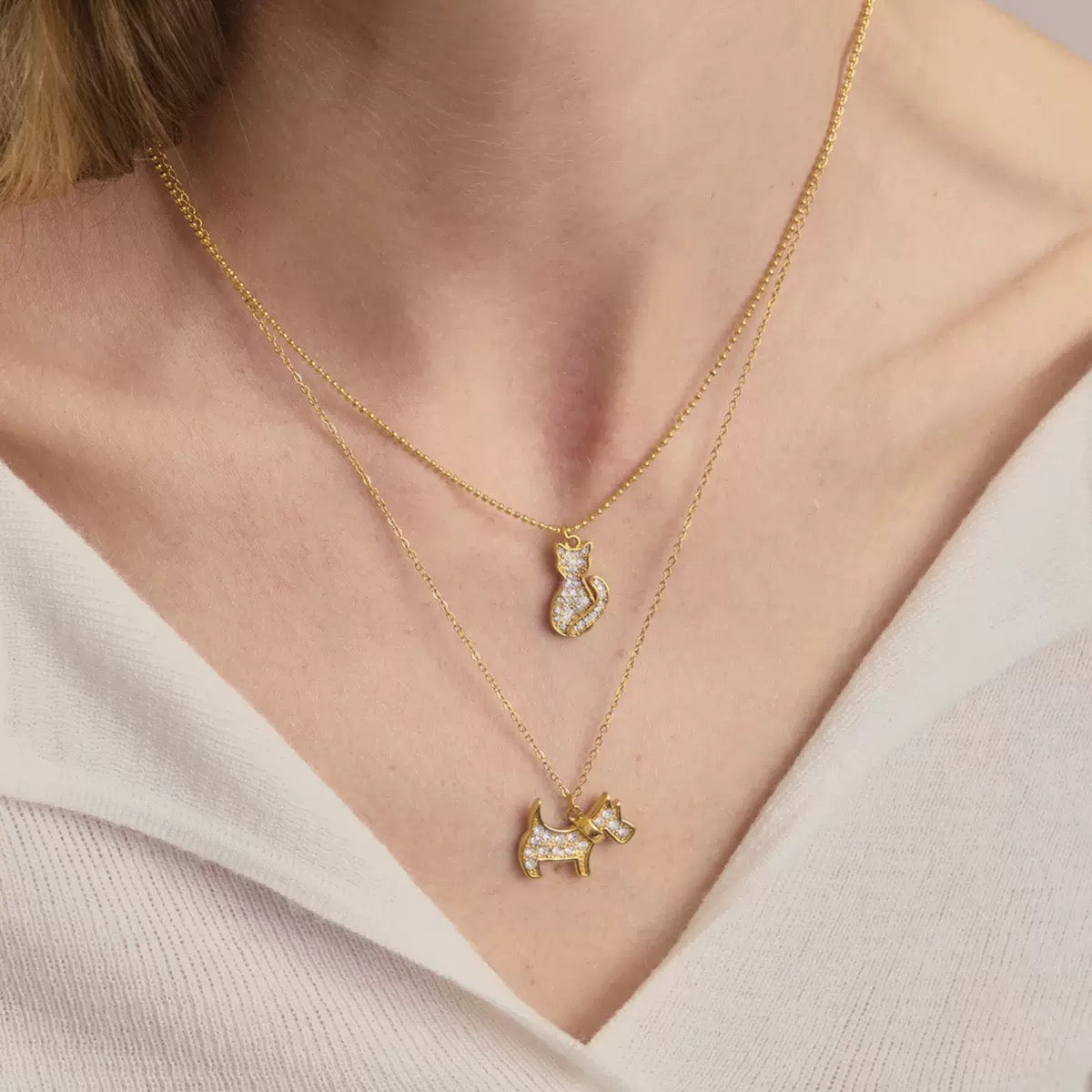 Gold necklaces with cat pendants on a person wearing a light-colored top.
