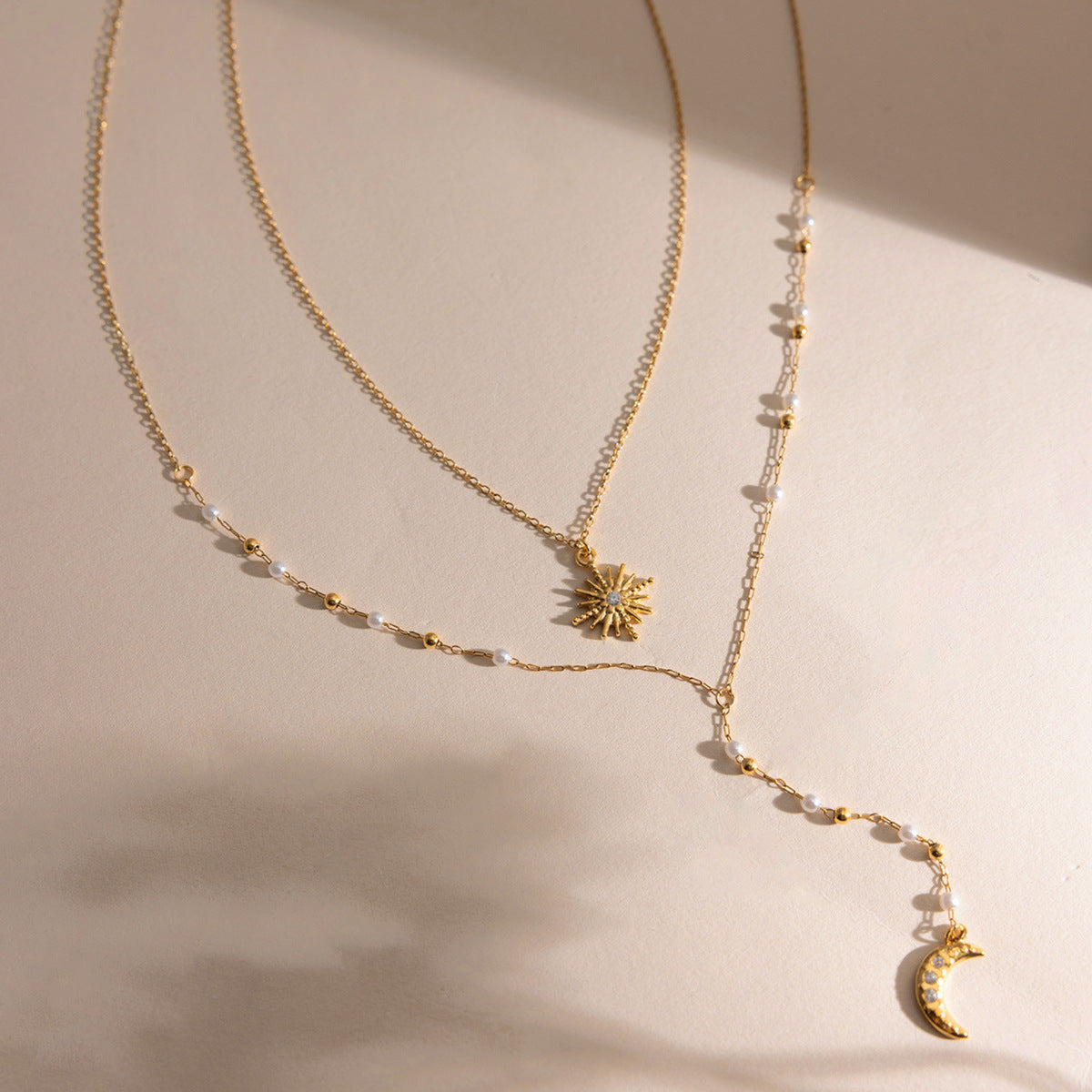 Gold necklace with sun and moon pendants on a beige background