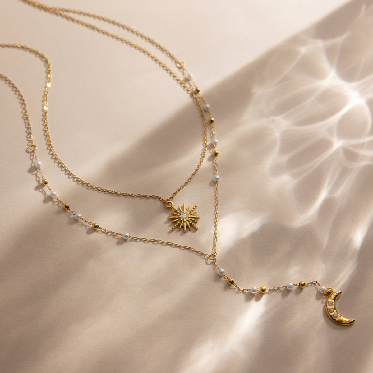 Gold necklace with star and moon pendants on a beige surface