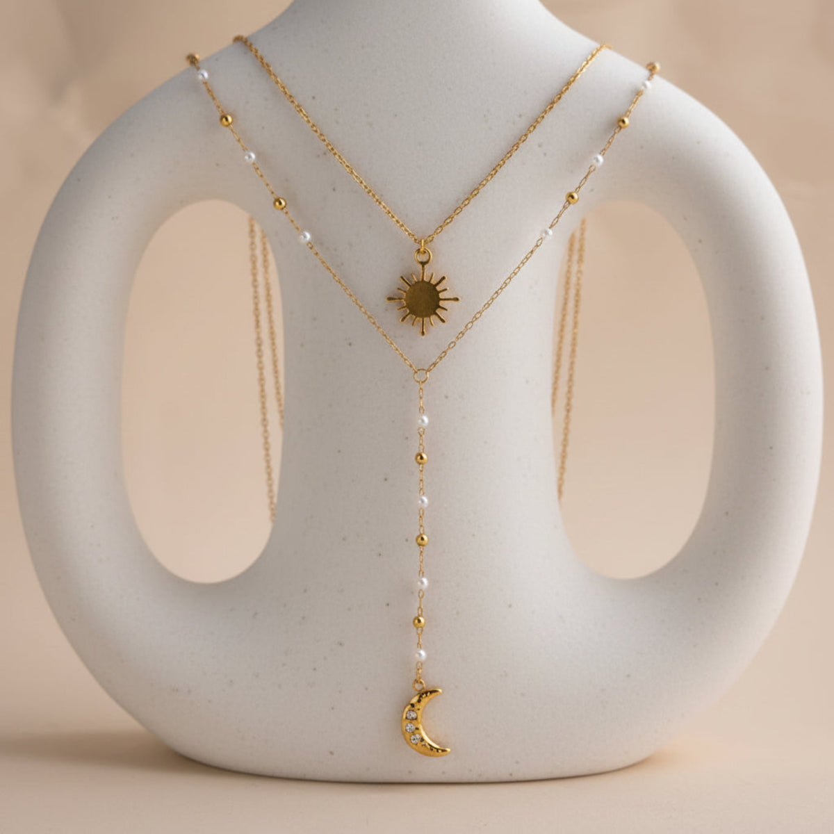 Gold necklace with sun and moon charms on a stone stand against a beige background